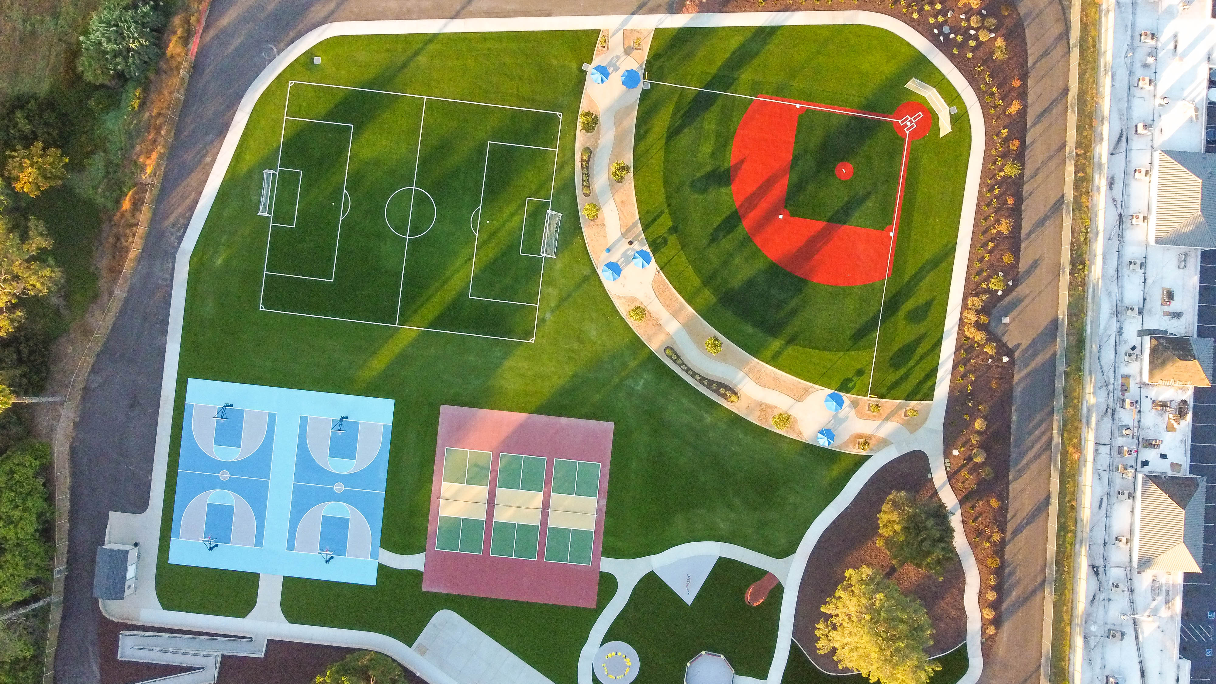 Aerial view of a completed multi-sport park with turf soccer field, baseball field, basketball courts and playground